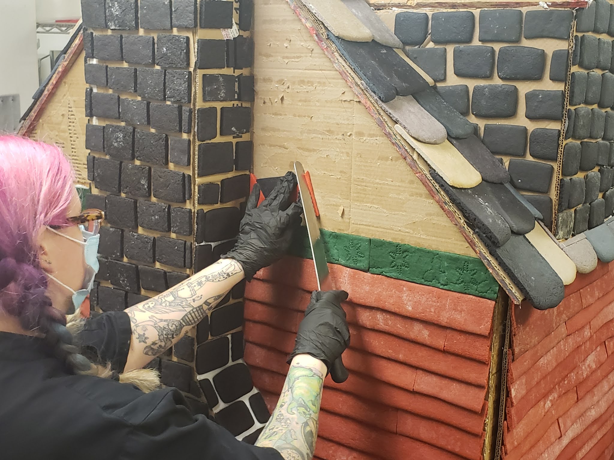 a person with tattoos using a spatula to put on a brick wall