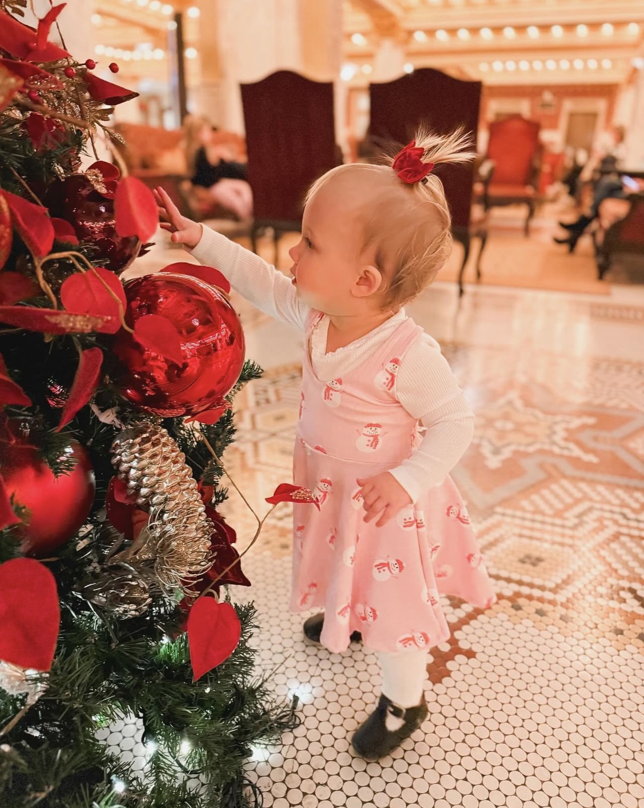 a baby girl standing next to a christmas tree