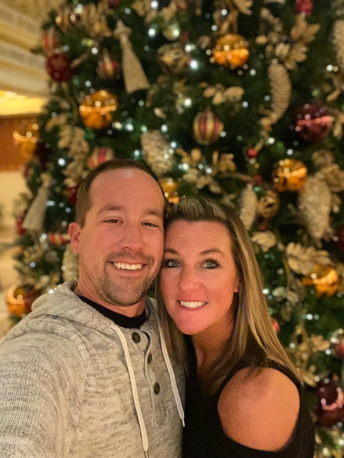 a man and woman taking a selfie in front of a christmas tree