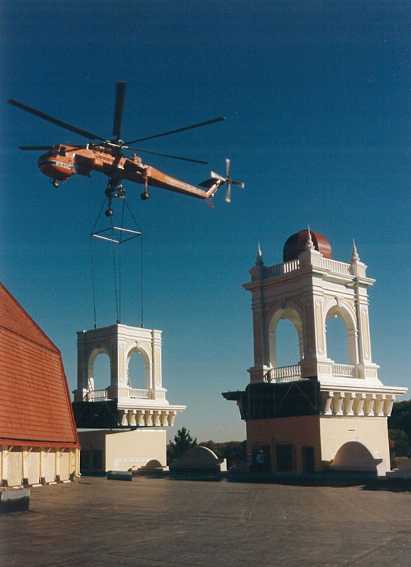 a helicopter carrying a load onto two white buildings