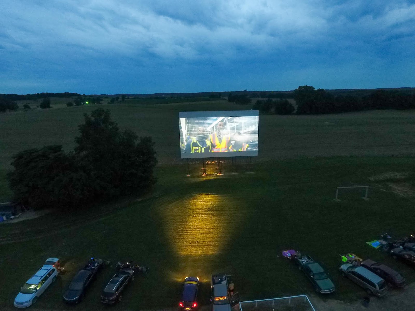 a screen in a field with cars parked in front of it